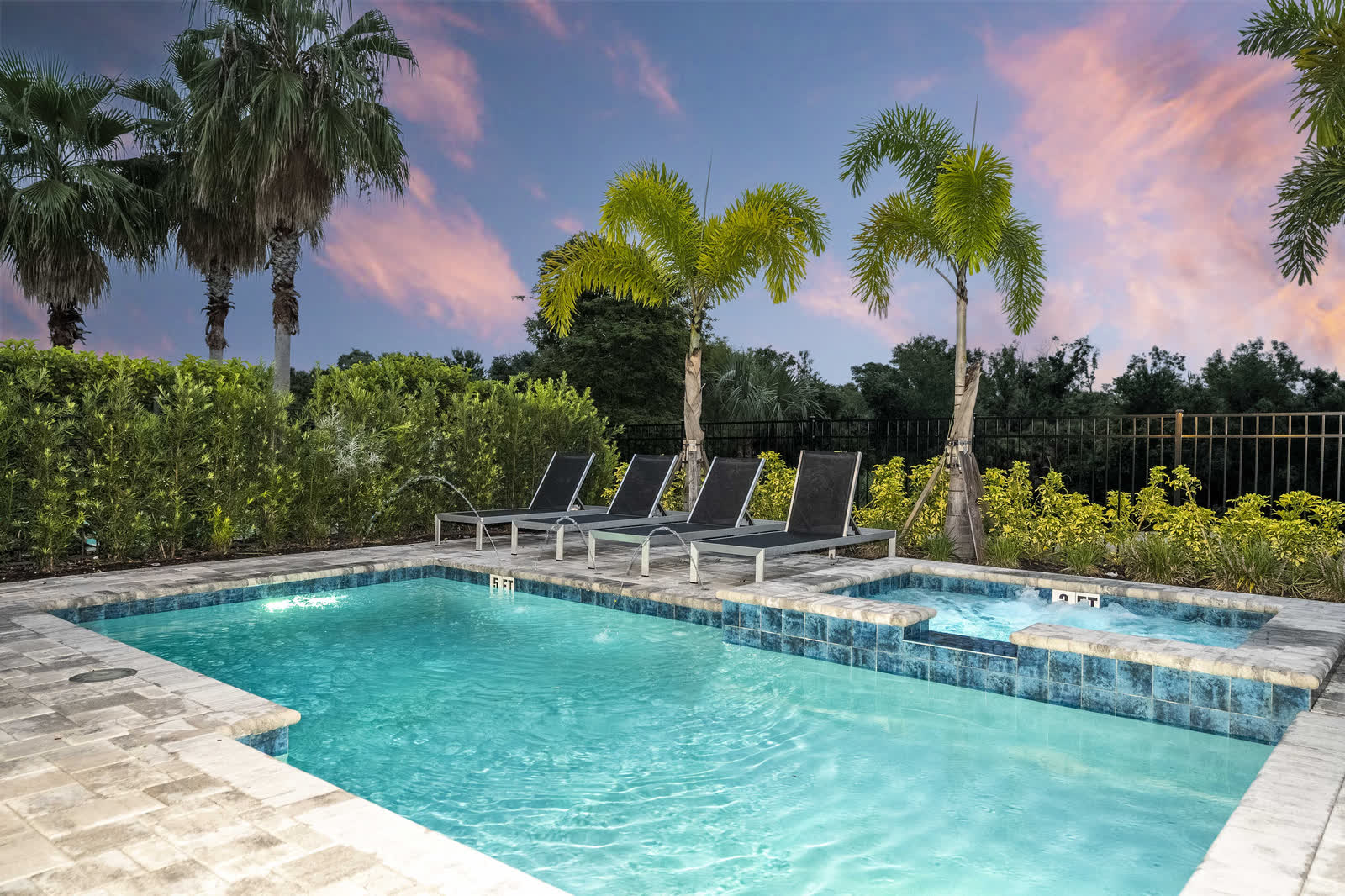 Vacation rental pool and hot tub at dusk, framed by palm trees